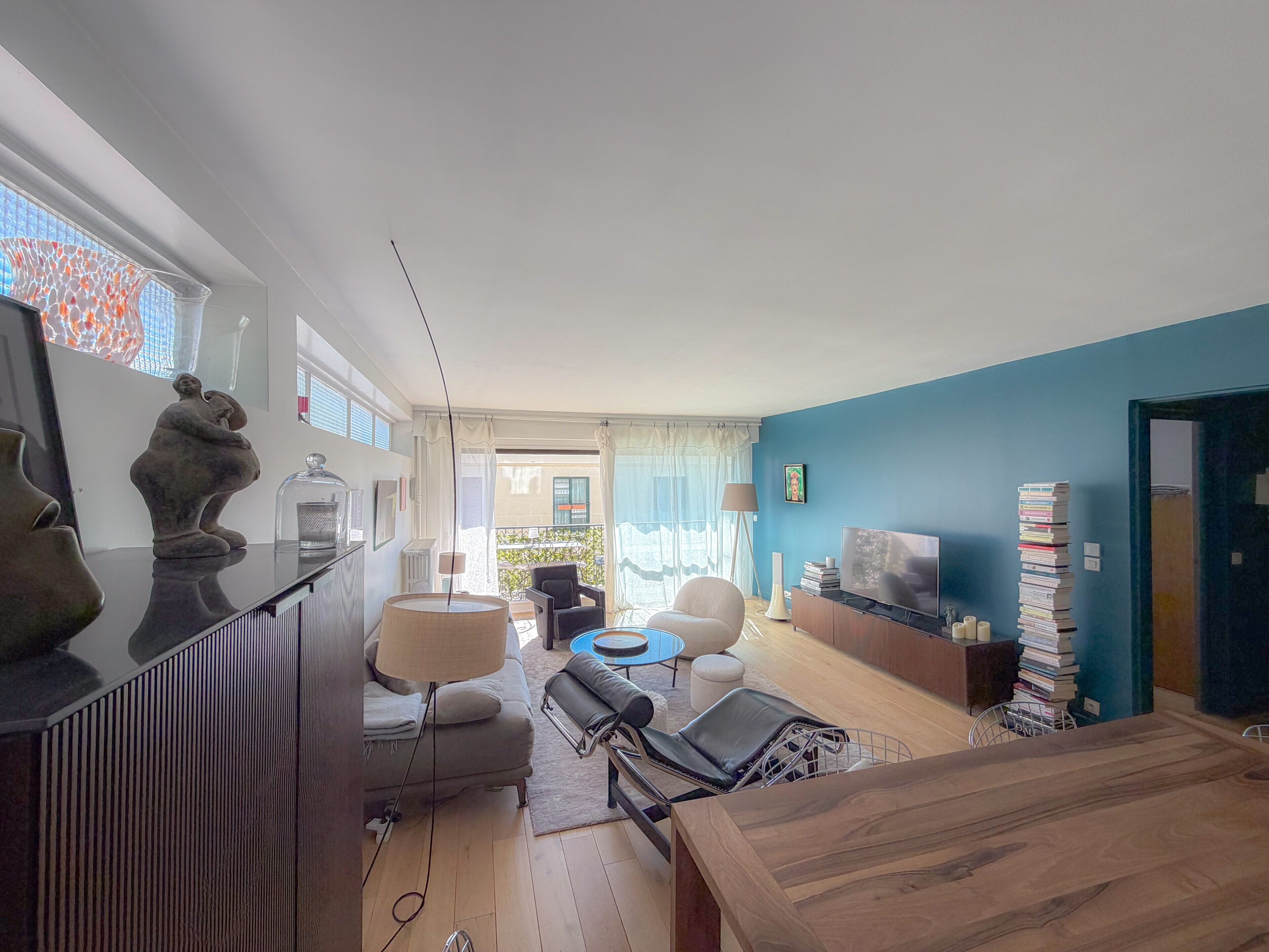 Un salon moderne avec un canapé, une table basse et un téléviseur. On y trouve également une table à manger avec des chaises et une lampe. La pièce est dotée d’une grande fenêtre qui offre une vue sur l’extérieur.