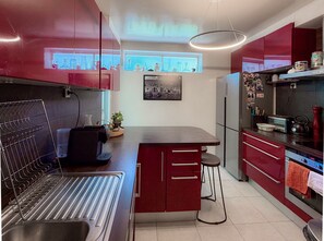 Eine moderne Küche mit roten Schränken, einer Edelstahl-Spüle, einem eingebauten Backofen und einer kleinen Kochinsel mit Sitzgelegenheiten.