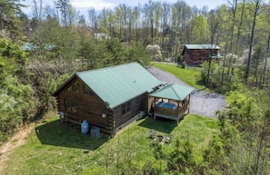 Eine Holzhütte mit einem grünen Metalldach, einem Whirlpool und einem eingezäunten Garten.