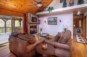 A cozy living room with a stone fireplace, leather sofas, and a ceiling fan. - Lazy Log Cabin at Raccoon Retreat (Whittier)