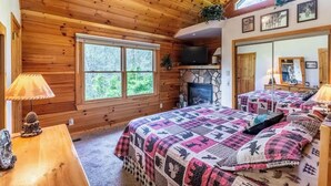A log cabin bedroom with a stone fireplace, a television, and a large window. - Lazy Log Cabin at Raccoon Retreat (Whittier)