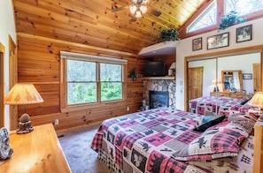 Ein Schlafzimmer in einer Blockhütte mit Kamin aus Stein, einem Fernseher und einem großen Fenster.
