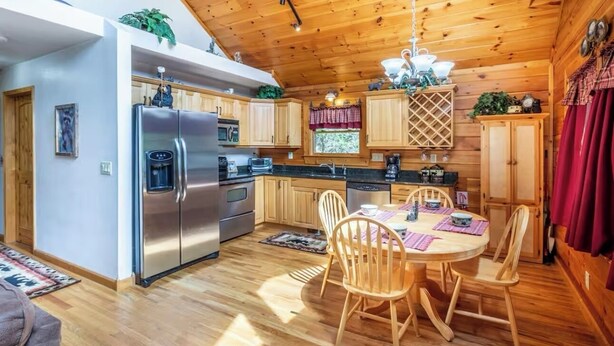 A wooden cabin interior with a kitchen, dining area, and a large window. - Lazy Log Cabin at Raccoon Retreat (Whittier)