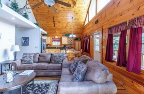 Ein gemütliches Cabin-Interieur mit Holzbalkendecke, einem Wohnbereich mit Sofa und Couchtisch, einer Küche mit Holzschränken und einem Essbereich mit Tisch und Stühlen.