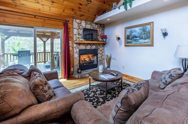 A cozy living room with a stone fireplace, comfortable seating, and a television. - Lazy Log Cabin at Raccoon Retreat (Whittier)