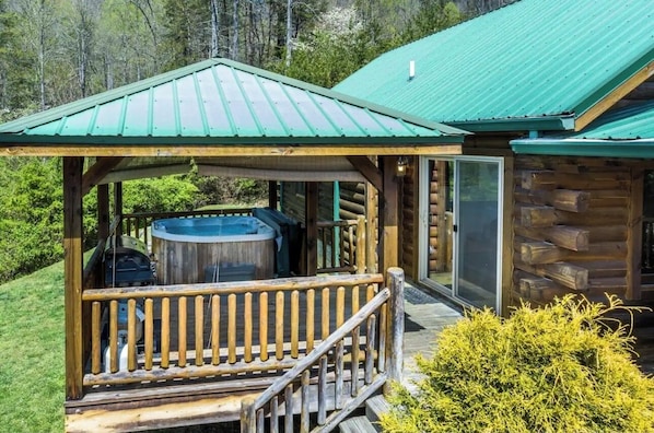 A log cabin with a covered porch, a hot tub, and a view of the surrounding forest. - Lazy Log Cabin at Raccoon Retreat (Whittier)
