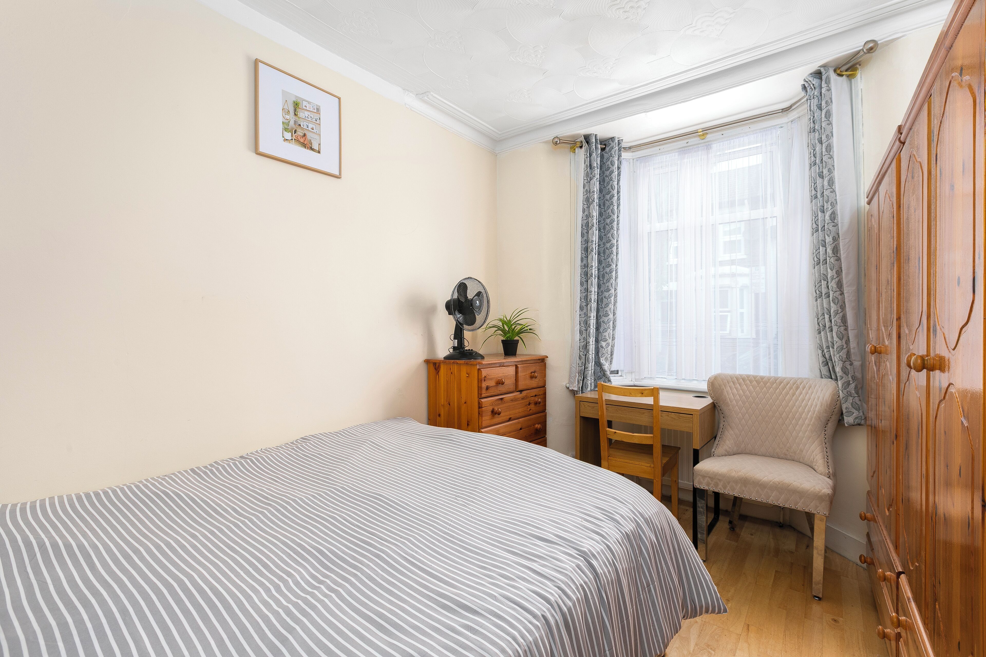 A bedroom with a bed, a desk, a chair, a dresser, and a door.