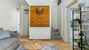 En stue med et rundt træbord, en grå sofa, et træur på væggen og en trappe til et andet rum.