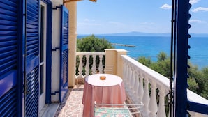 Ein Balkon mit Tisch und Stühlen, mit Blick auf ein Gewässer und grüne Vegetation.