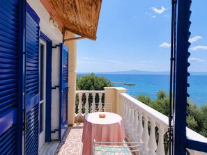 Ein Balkon mit Tisch und Stühlen, mit Blick auf ein Gewässer und grüne Vegetation.