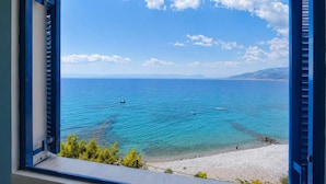 Blick auf die Küste durch ein Fenster mit blauen Fensterläden, klares blaues Meer und ein Sandstrand.
