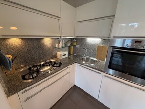 A modern kitchen with white cabinets, a granite countertop, stainless steel appliances, and a built-in oven. - Casa Mare - Panoramic View of the Ligurian Sea (San Lorenzo al Mare)