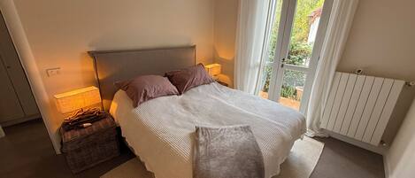 A bedroom with a bed, bedside lamps, a basket, and a view through a window.