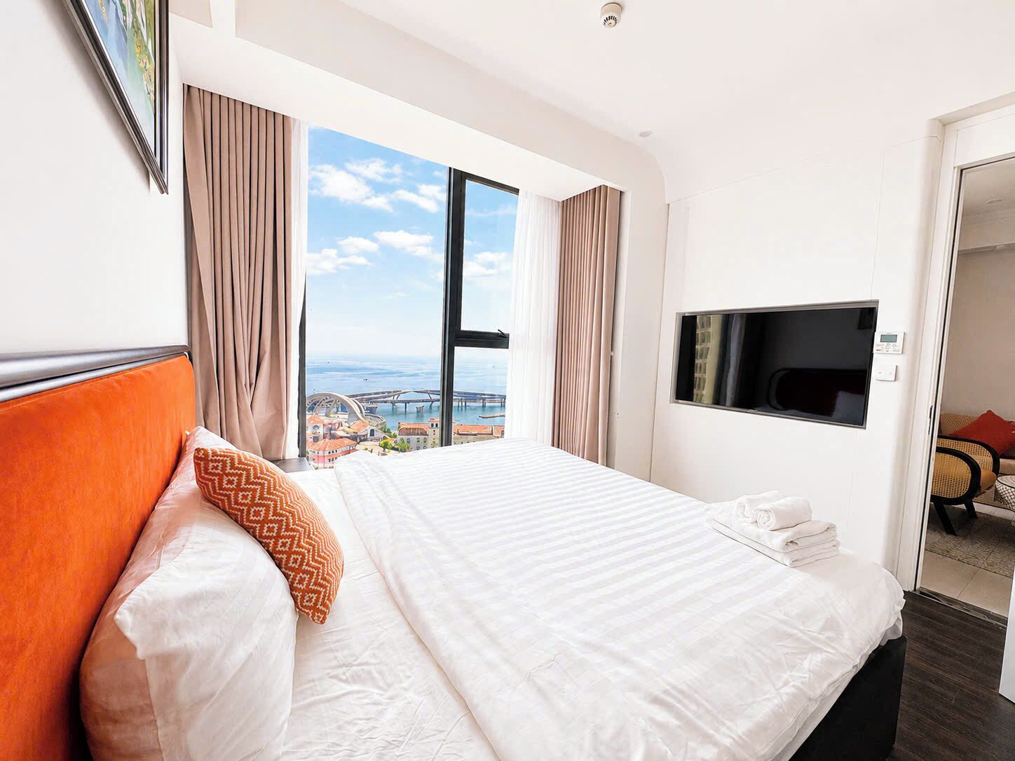 Quarto de hotel com uma cama grande, televisão e vista para a cidade pela janela.