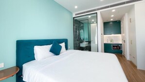 A modern bedroom with a large bed, a nightstand, a glass shower enclosure, and a bathroom with a sink and mirror.