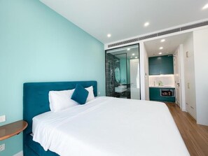 A modern bedroom with a large bed, a nightstand, a glass shower enclosure, and a bathroom with a sink and mirror.