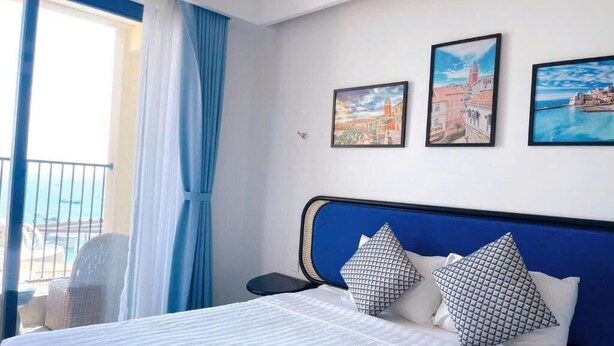 A hotel room with a bed, a nightstand, a chair, and a view of the sea through a window.