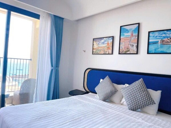 A hotel room with a bed, a nightstand, a chair, and a view of the sea through a window.