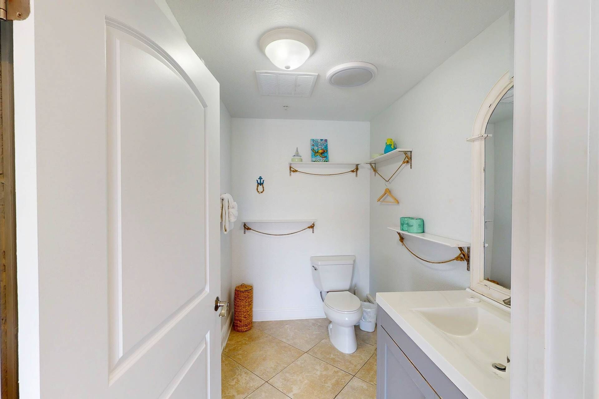 A bathroom with a toilet, a sink, and shelves with toiletries.