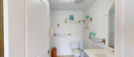 A bathroom with a toilet, a sink, and shelves with toiletries.