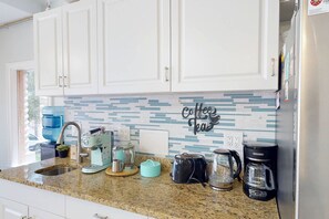 A kitchen with white cabinets, a coffee-themed backsplash, and various appliances including a coffee maker, toaster, and kettle. - Private Elevator, Spectacular Pool & Marina Views, Steps to Madeira Beach & John's Pass Village (Madeira Beach)