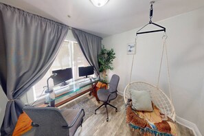 A modern room with a glass desk, two monitors, a grey office chair, a hanging chair with a colorful cushion, and a potted plant. - Private Elevator, Spectacular Pool & Marina Views, Steps to Madeira Beach & John's Pass Village (Madeira Beach)