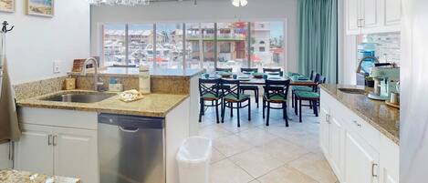 A kitchen with a dishwasher, a dining area with chairs, a ceiling fan, and a view of a marina through large windows.