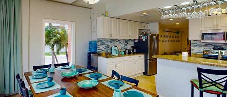A modern kitchen with white cabinets, a central island, and a dining area with a wooden table set for six.
