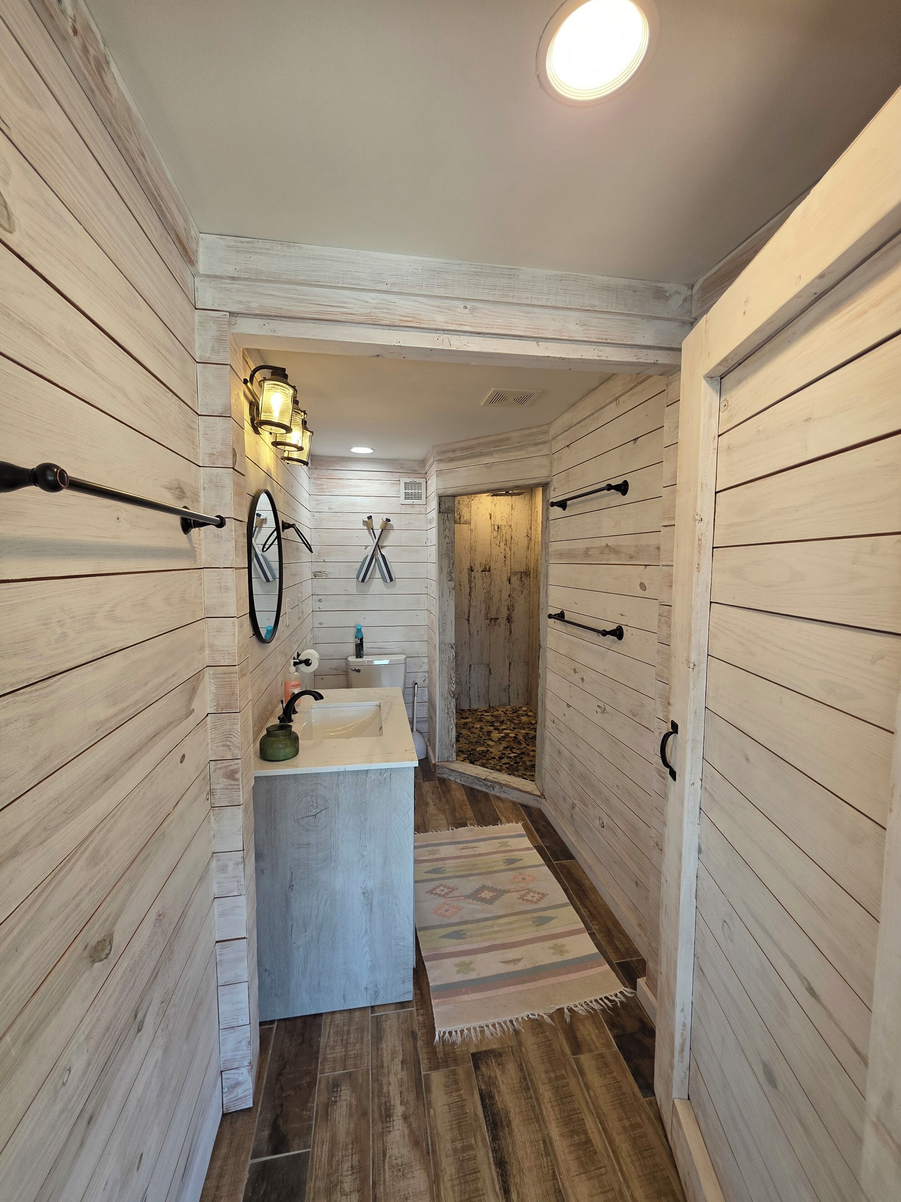Ein schmaler Flur mit Holzwänden, einem kleinen Waschbecken, einer Toilette und einem Duschbereich.