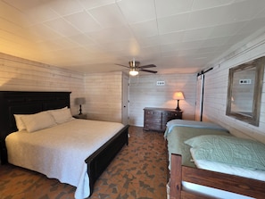 A bedroom with a large bed, a smaller bed, a dresser, a ceiling fan, and a window with a mirror. - Wonderful 5-bedroom Lake House on Lake Martin (Equality)