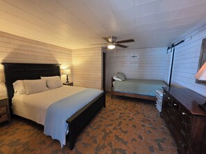 Une chambre à coucher comprenant un lit, une table de chevet, une commode, un ventilateur de plafond et une fenêtre.