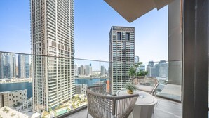 Ein Balkon mit Blick auf hohe Gebäude, ein kleiner Tisch mit einer Pflanze und ein Korbstuhl.
