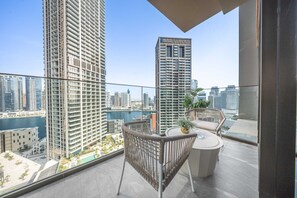 A balcony with a view of high-rise buildings, a small table with a plant, and a wicker chair. - Free Housekeeping Visits During Your Stay - Stayshort - Studio in Business Bay Sleeps 2 With Burj Views (Dubai)