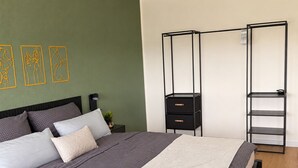 Un dormitorio con cama, mesita de noche, unidad de almacenamiento metálica negra con cajones y estante fijado a la pared.