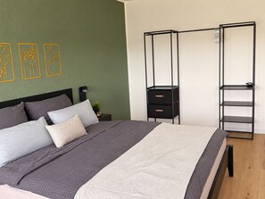 Una camera da letto con un letto, un comodino, un contenitore in metallo nero con cassetti e una mensola a parete.