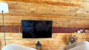 A room with a wooden ceiling, a flat-screen TV mounted on the wall, two bean bags, a small table with a lamp, and a decorative vase. - Country house for relaxation!! 3 bedrooms, swimming pool, fishing lake, fully equipped kitchen. (Cambuí)
