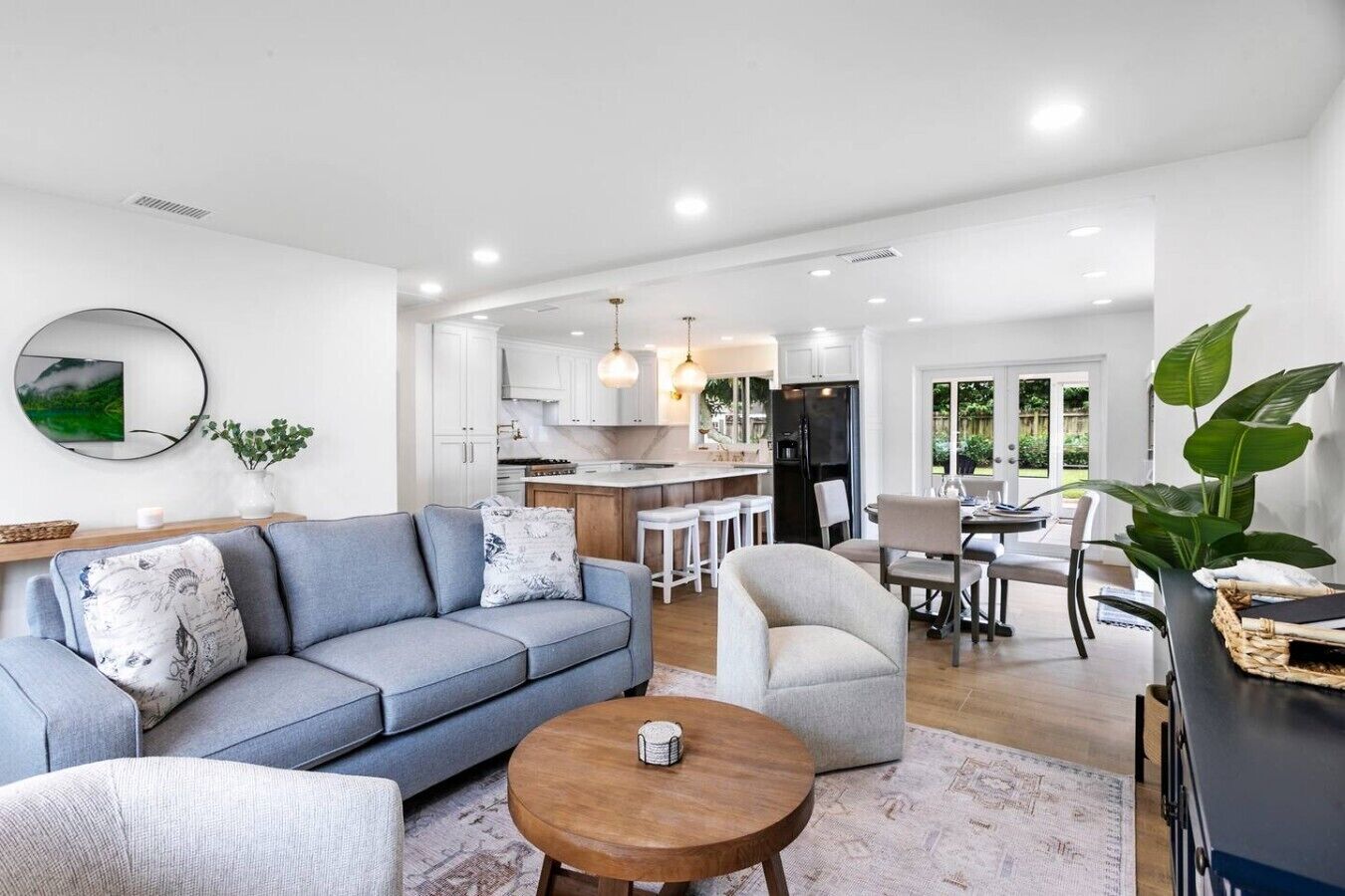 A modern living room with a grey sofa, a round coffee table, and a dining area with a white table and chairs.