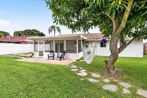 A house with a covered patio, two chairs, a hammock, and a tree. - 3BD/2BA Palm Gardens Retreat (Palm Beach Gardens)