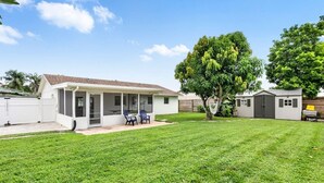 Une maison de plain-pied avec un patio couvert, une cour clôturée et un arbre.