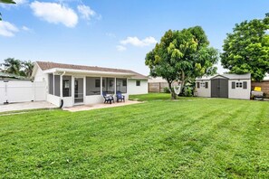 A single-story house with a covered patio, a fenced yard, and a tree. - 3BD/2BA Palm Gardens Retreat (Palm Beach Gardens)