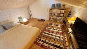 Una camera da letto mansardata accogliente con un letto, un tappeto decorato, una libreria e una televisione.