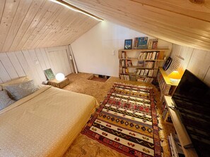 A cozy attic bedroom with a bed, a patterned rug, a bookshelf, and a television. - Country house with a large garden – 10 minutes from the beaches and 5 minutes from O'Fun Park (Avrillé)