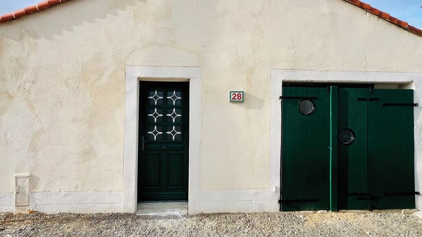 Un edificio con facciata beige, una porta verde e un tetto in tegole rosse.