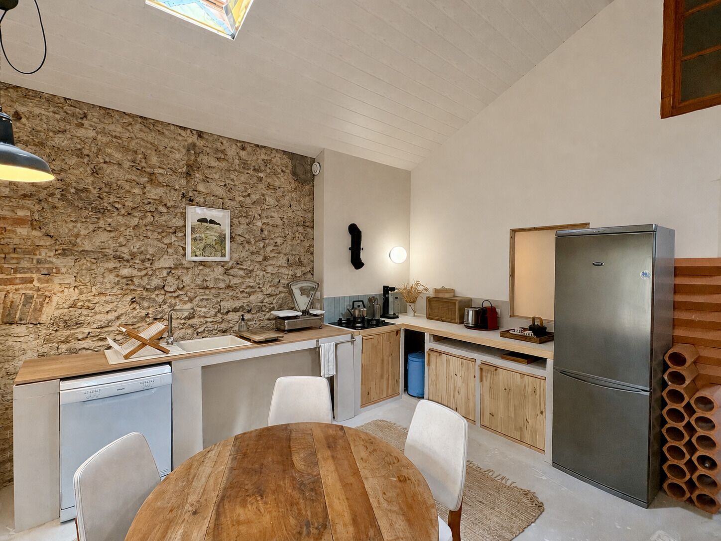 A compact kitchen with a stone wall, wooden cabinets, a stainless steel refrigerator, and a dining area with a wooden table and chairs.