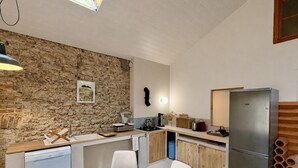 Una cucina funzionale con parete in pietra, pensili in legno, frigorifero in acciaio inossidabile e zona pranzo con tavolo e sedie in legno.