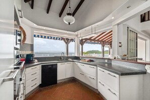 A modern kitchen with a view of the sea, featuring white cabinets, a black dishwasher, and a large island with a sink. - Villa Grand Large - Four Bedroom Villa, Sleeps 8 (Les Trois-Îlets)