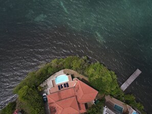 Eine Luftaufnahme eines Küsteneigentums mit Schwimmbad, einem Gebäude mit rotem Dach und einem hölzernen Steg, der ins Wasser führt.