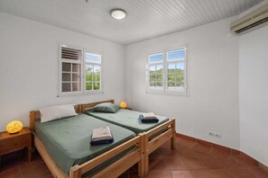 A room with two beds, a window, a nightstand, and an air conditioning unit. - Villa Grand Large - Four Bedroom Villa, Sleeps 8 (Les Trois-Îlets)
