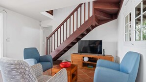 Ett vardagsrum med en trätrappa, två blå fåtöljer, en mönstrad soffa, ett soffbord och en tv som står på ett träställ.