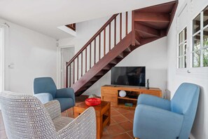 Ein Wohnzimmer mit einer Holztreppe, zwei blauen Sesseln, einem gemusterten Sofa, einem Couchtisch und einem Fernseher auf einem Holzboden.